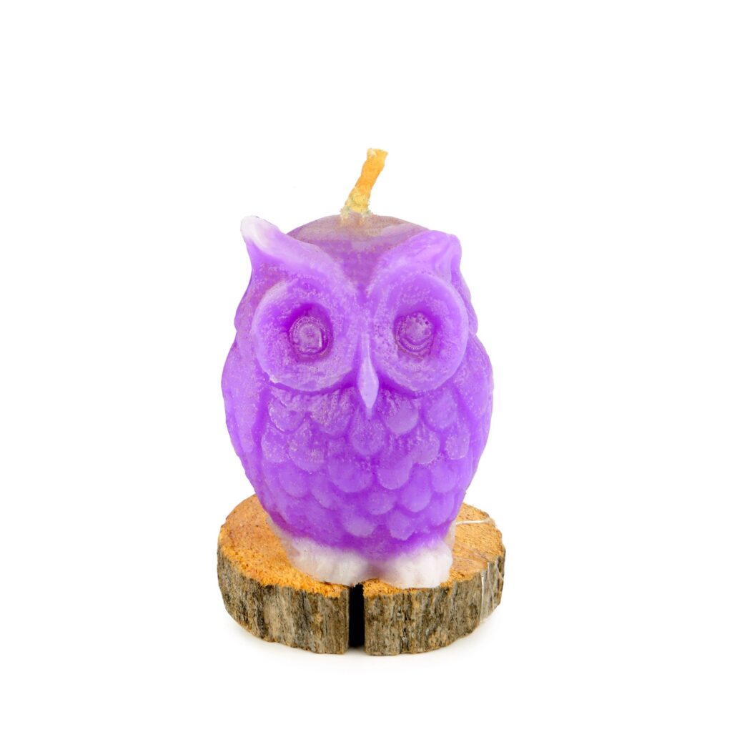 Purple owl shaped candle on a wooden pedestal isolated on white
