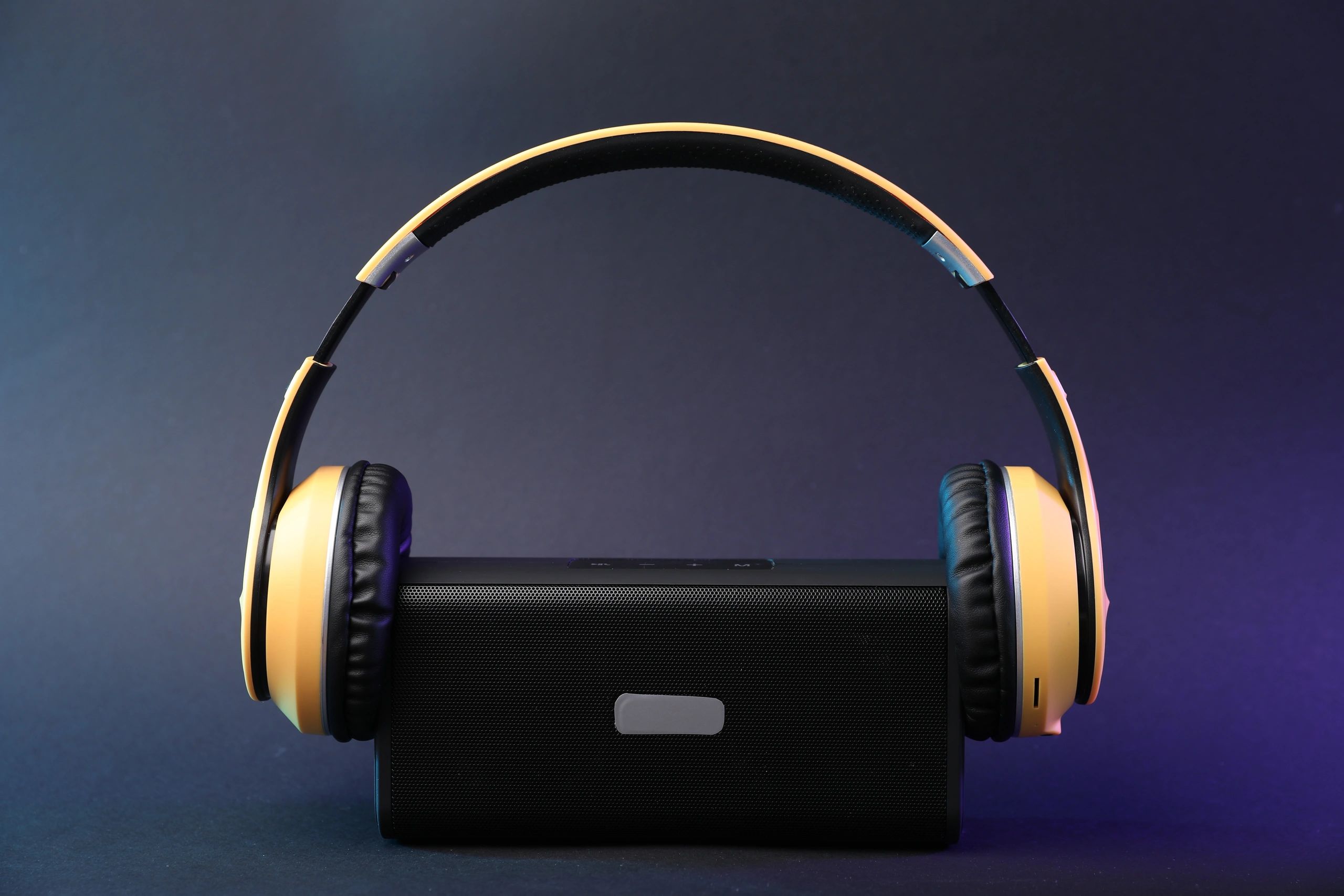 Headphones and portable bluetooth speaker on dark gray background