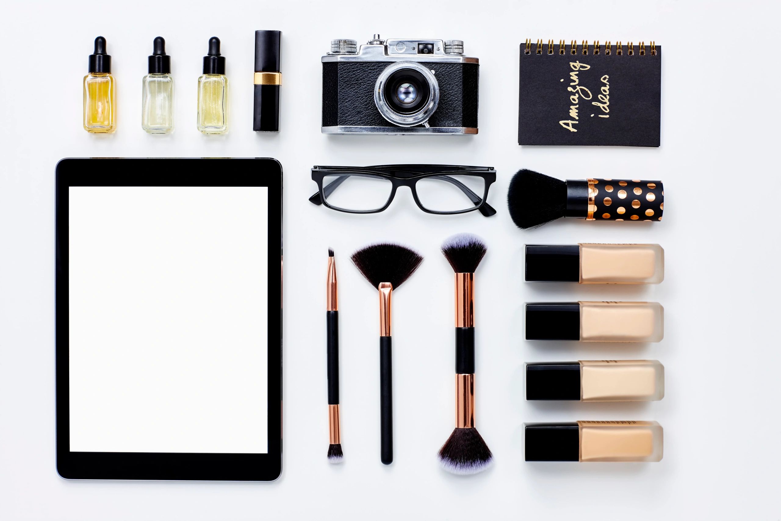 Flat lay of beauty products arranged around a tablet on white background